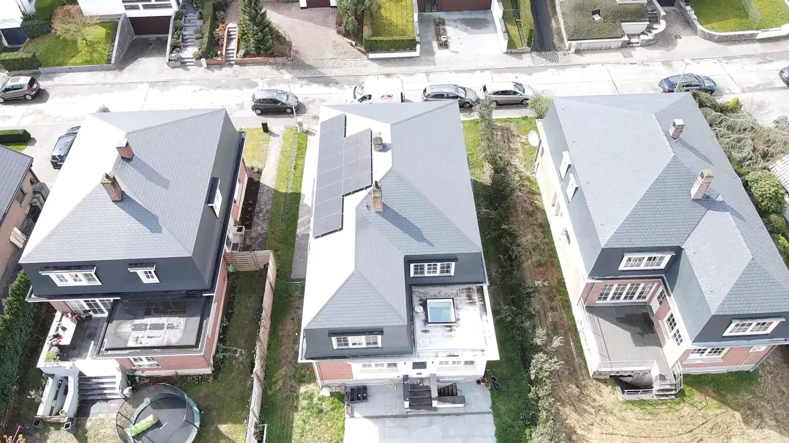 Luchtfoto van drie woningen met grijze hellende daken, op één ervan liggen zonnepanelen