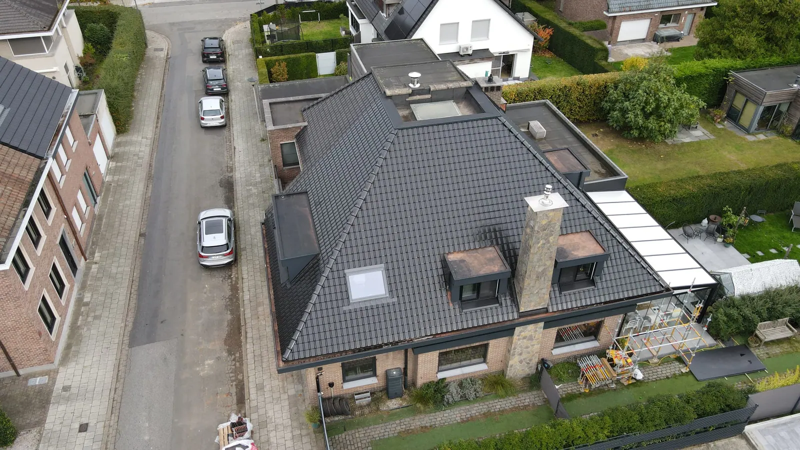 Luchtfoto van een woning met een antracietkleurig pannendak, een stenen schoorsteen, twee dakkapellen en een dakvenster